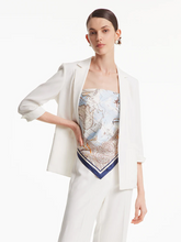 a lady wearing a silk scarf as a top with a white blazer and white pants